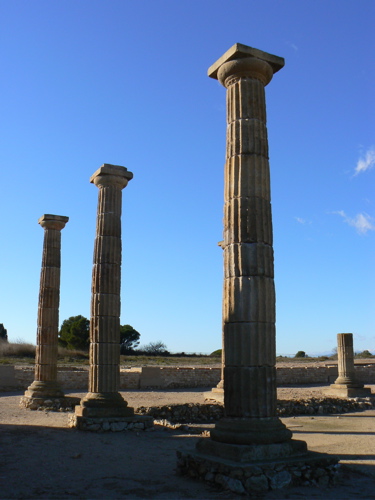 Three ancient columns in a ruined city against a blue summer sky