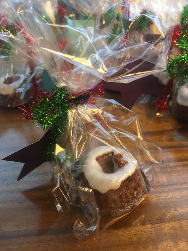 A little ring-shaped cake with icing on it inside a cellophane bag with red and green tinsel and a star gift tag.
